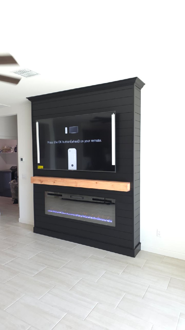 Black shiplap TV wall with wood mantle blue LED fireplace and white tile floor Arizona